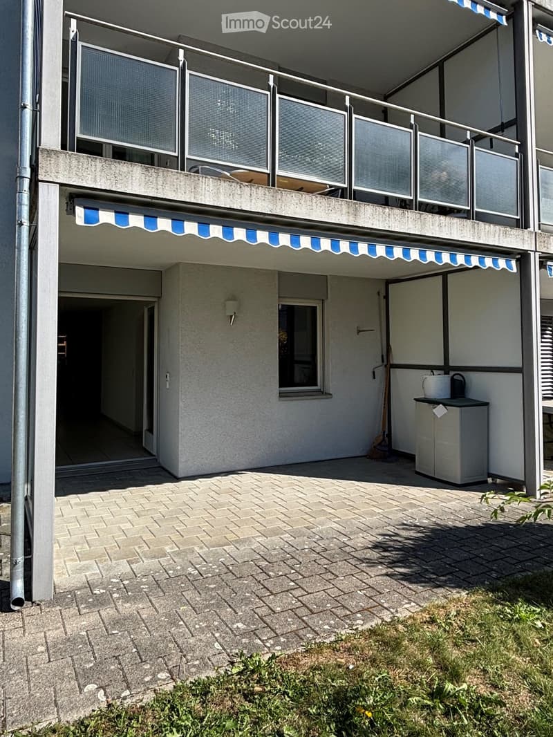 Balcony with striped awning, metal railings, and a small storage area with a broom and bucket.