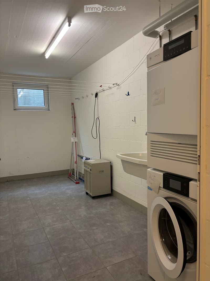 Laundry room with a washing machine, sink, laundry basket, and laundry rack. The room has a tiled floor and white brick walls.