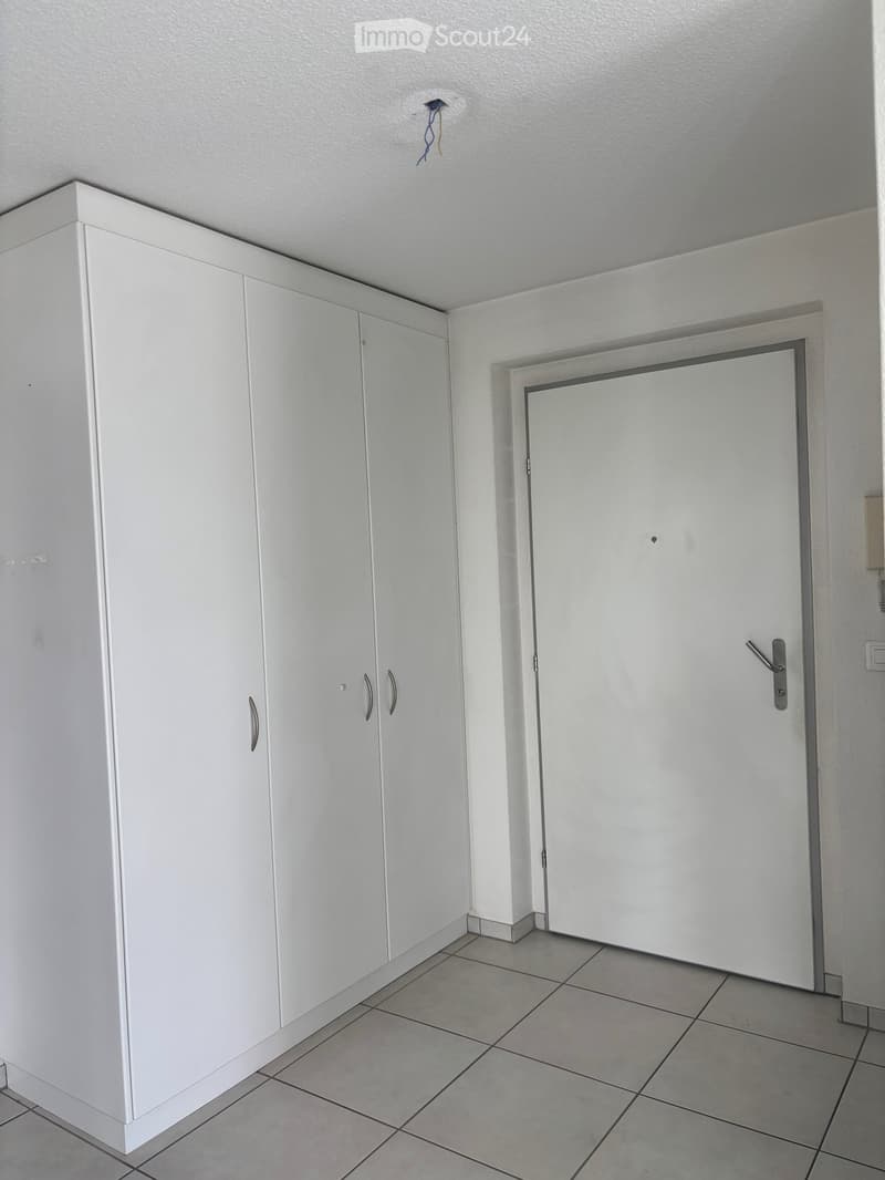 Empty room with white tiled floor, white built-in cabinets, and a closed white door.