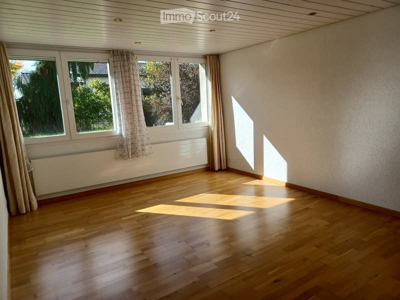 Empty room with wooden flooring, large windows with curtains, radiator, and natural light from outside.