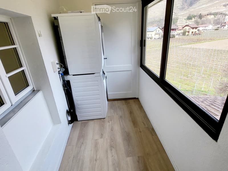 Empty room with wooden flooring, white walls, and large windows offering a view of the countryside.