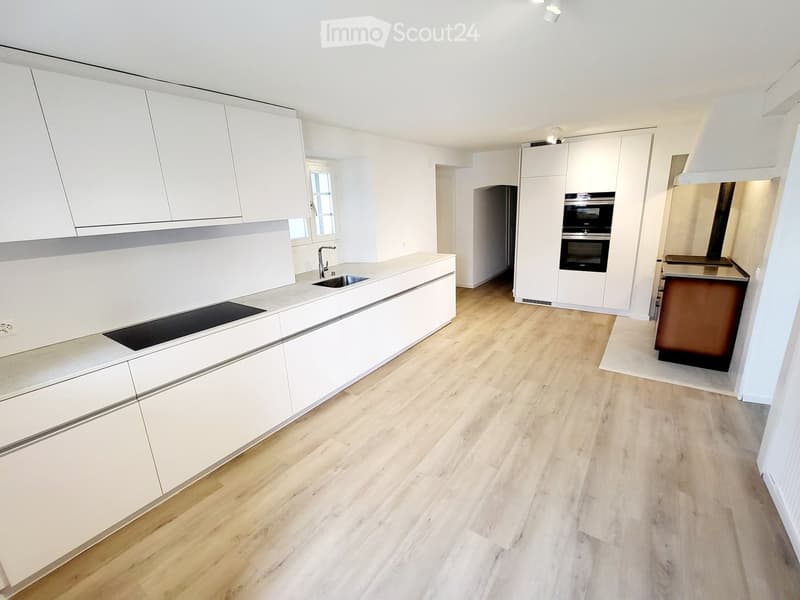 Modern kitchen with white cabinets, wooden flooring, and built-in appliances including a sink, faucet, and oven.
