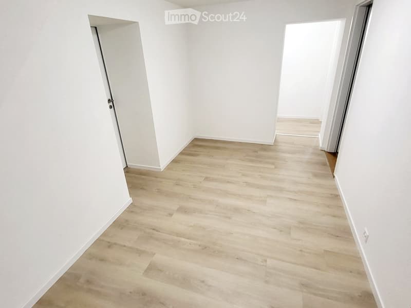 Empty hallway with light wooden flooring and white walls, featuring two open doorways on either side.