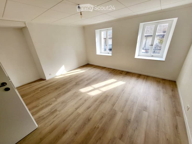 Empty room with wooden flooring and white walls, featuring two windows and a visible light fixture on the ceiling.
