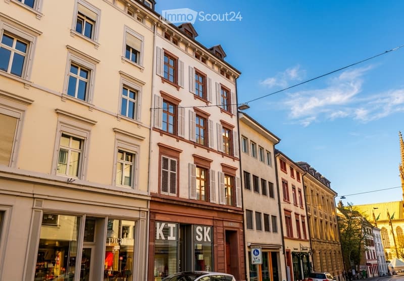 A row of multi-story buildings with classic European architecture, featuring large windows, shutters, and storefronts on the ground floor.