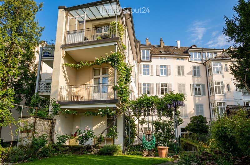 Multi-story residential building with balconies, greenery, and a well-maintained garden area.