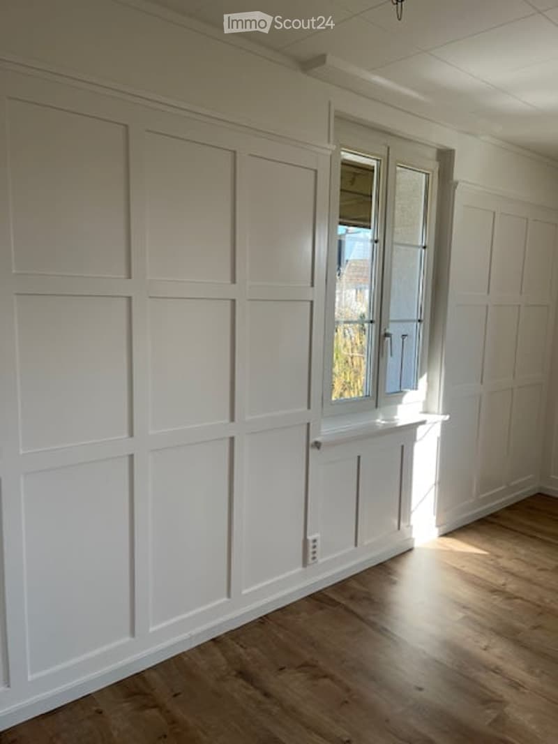empty room with white wooden panels, windows, wooden floor