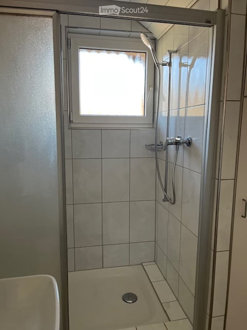 Small bathroom with walk-in shower, white tiles, silver shower fixtures, shower drain, white sink, small window