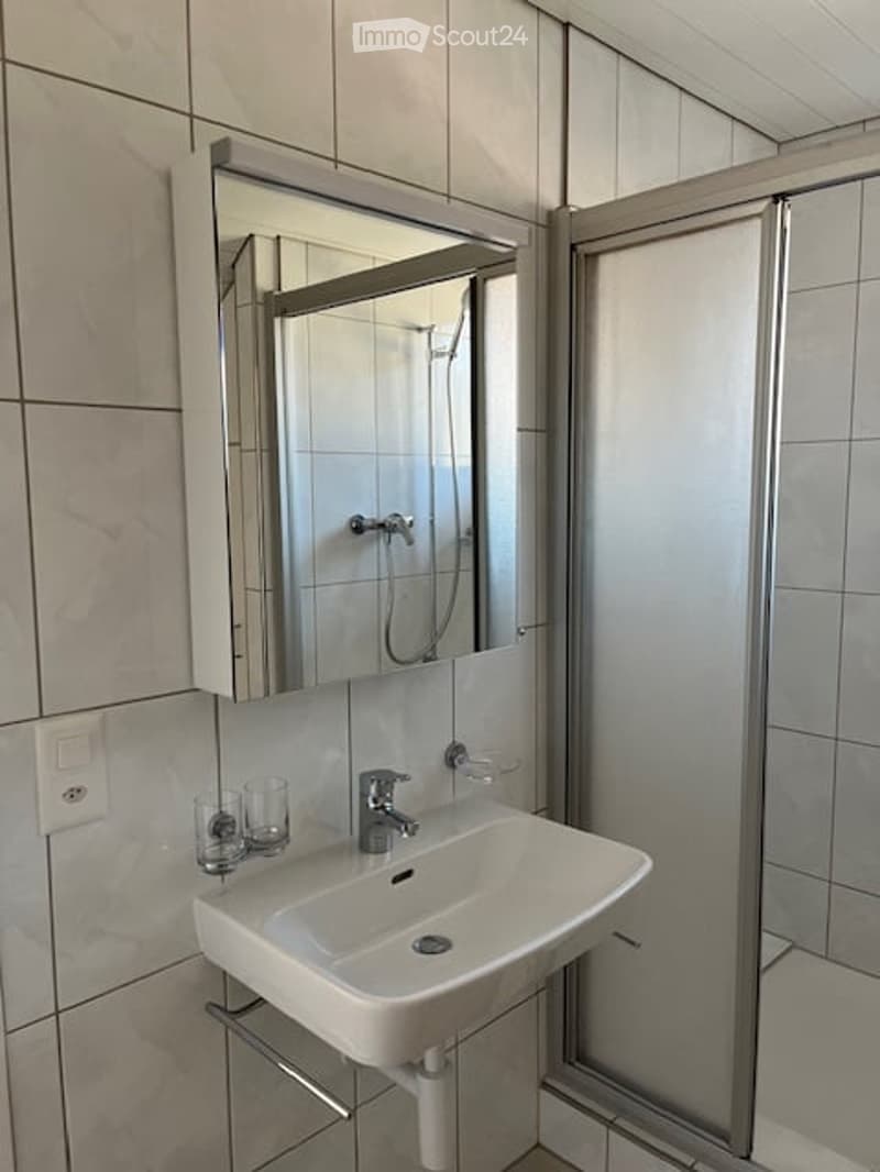 white tile walls, modern sink, glass shower enclosure, mirror, power outlet