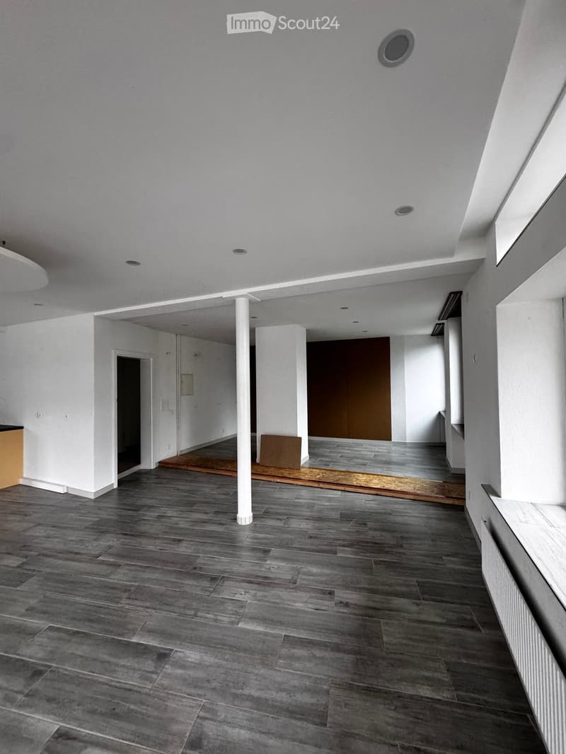 Empty room with grey wooden flooring, white walls, and a white column. There are no visible furnishings or decorations.