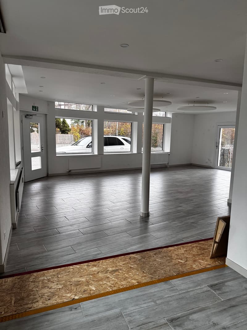 Empty room with wooden flooring, large windows, and a central column. No furniture or equipment present.