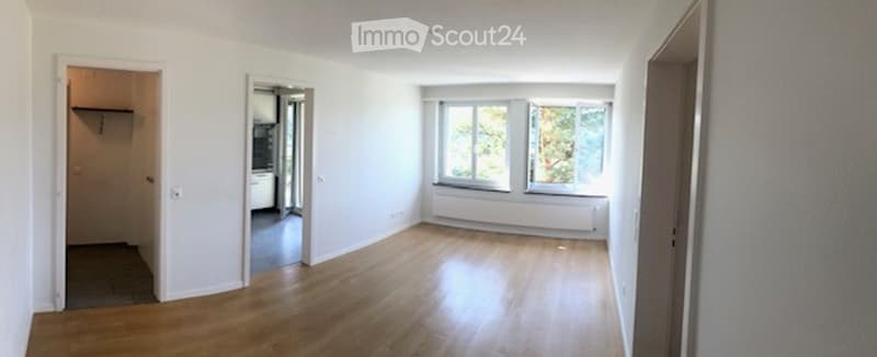 Empty room with light wooden flooring, white walls, and large windows. No furniture or equipment present.