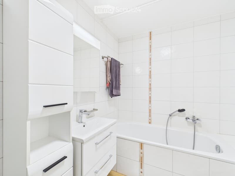 Modern bathroom with white tiles, a sink, a bathtub, and a towel hanging on a rack.