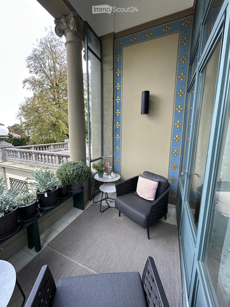 Balcony with a grey wicker chair, small round table, potted plants, and decorative wall panels.