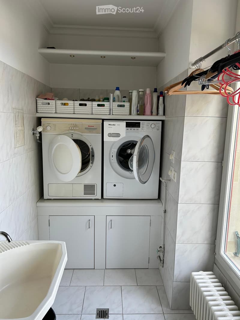 Modern bathroom with a washing machine, dishwasher, sink, radiator, and storage bins for cleaning supplies.