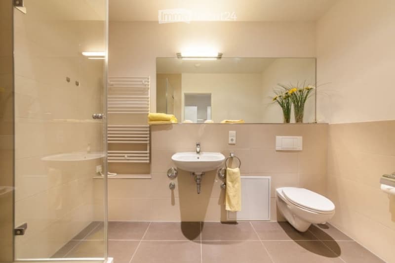 Modern bathroom with a white sink, toilet, large mirror, towel, and a glass-enclosed shower area.
