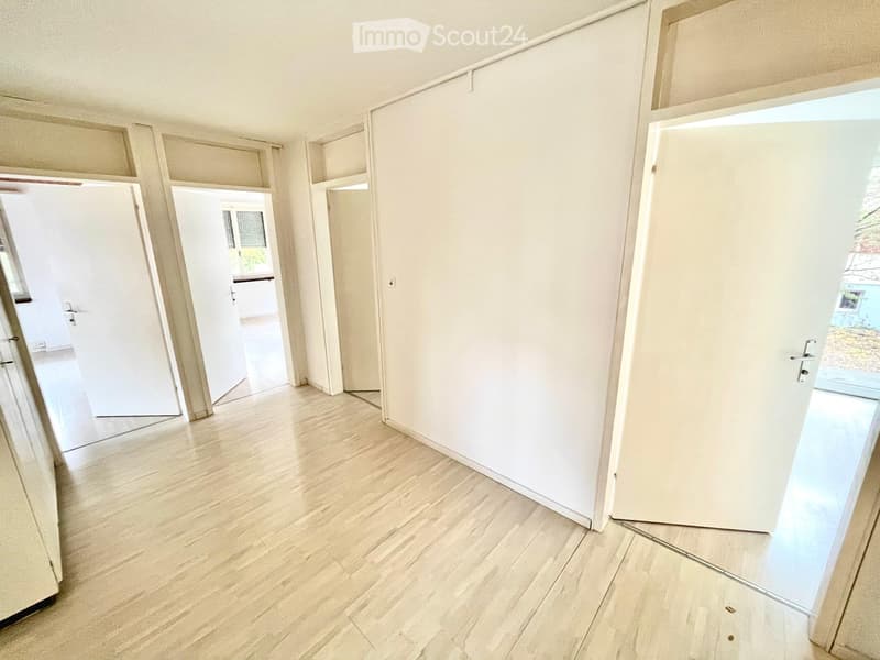Empty hallway with light wooden flooring and white walls, featuring several open doors leading to other rooms.