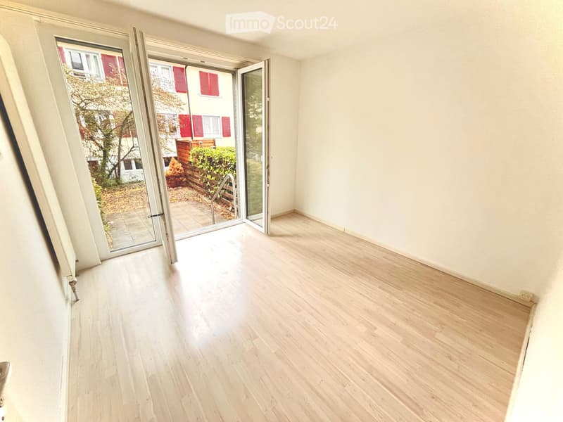 Empty room with light wooden flooring, white walls, and large sliding glass doors leading to a patio area.