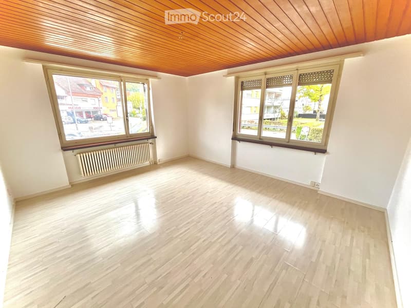 Empty room with light wooden flooring, white walls, large windows, and a radiator. No furniture or equipment present.