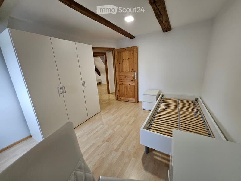 Modern, minimalist bedroom with light wooden flooring, white wardrobe, bed frame, and nightstand.