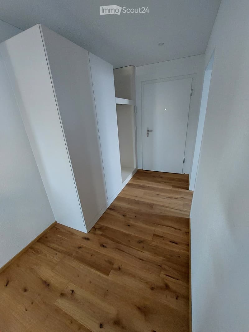 Empty hallway with wooden flooring, white walls, and a closed door at the end.