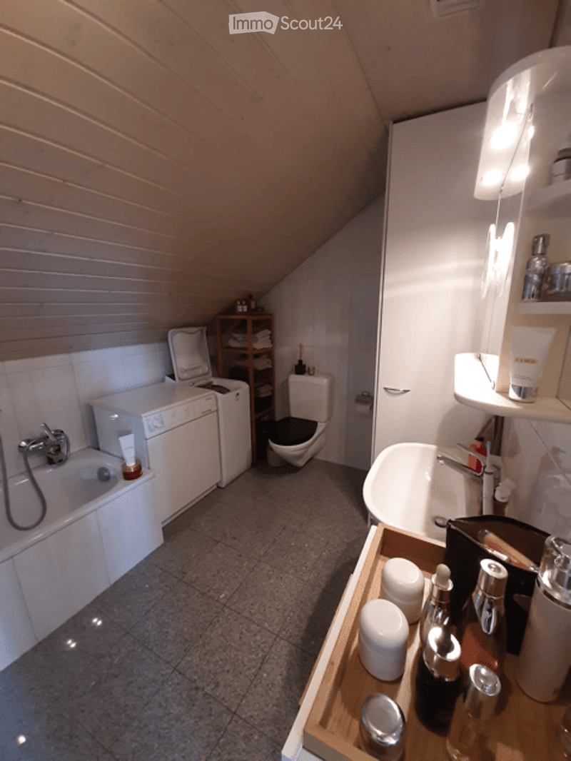 Modern bathroom with a bathtub, toilet, washing machine, and a wooden shelf holding toiletries and cosmetics.