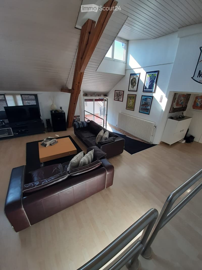 Modern living room with wooden flooring, a large sectional leather sofa, a wooden coffee table with books, a TV, and framed pictures on the walls.