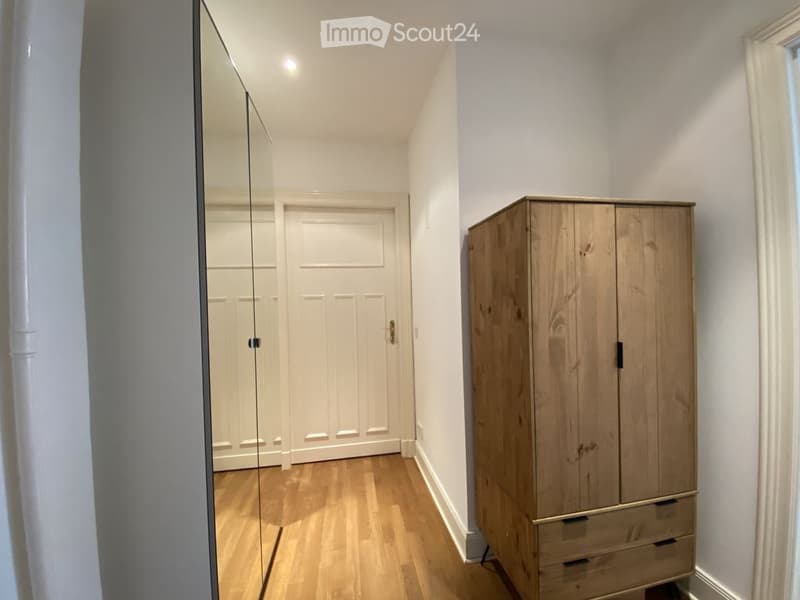 A narrow hallway with wooden flooring, a large mirrored wardrobe, and a closed door at the end.