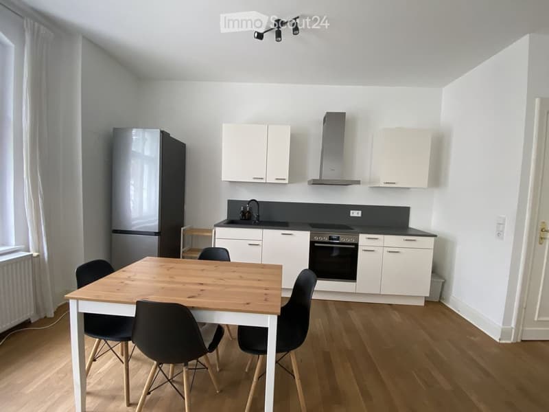Modern kitchen with white cabinets, stainless steel appliances, a wooden dining table with four chairs, and a sink with a faucet.
