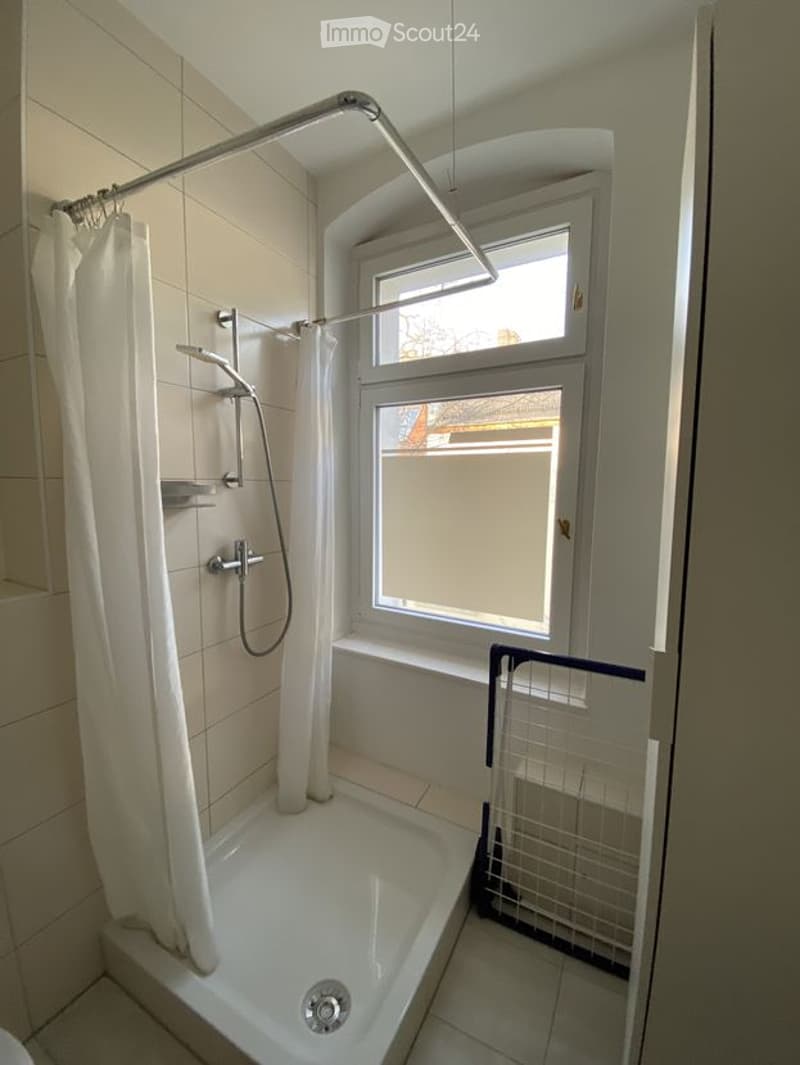 Bathroom with a bathtub, shower curtain, shower rod, and a window providing natural light.