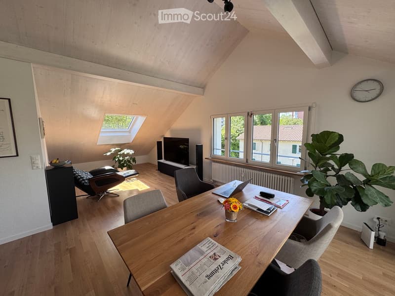 Bright, multi-functional room with wooden flooring, large windows, skylight, and modern furniture including a desk, chairs, laptop, and decorative plants.