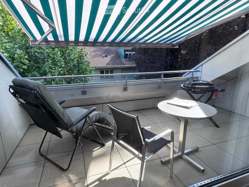 Balcony with tiled floor, metal railing, lounge chair, dining chair, small table, and grill.