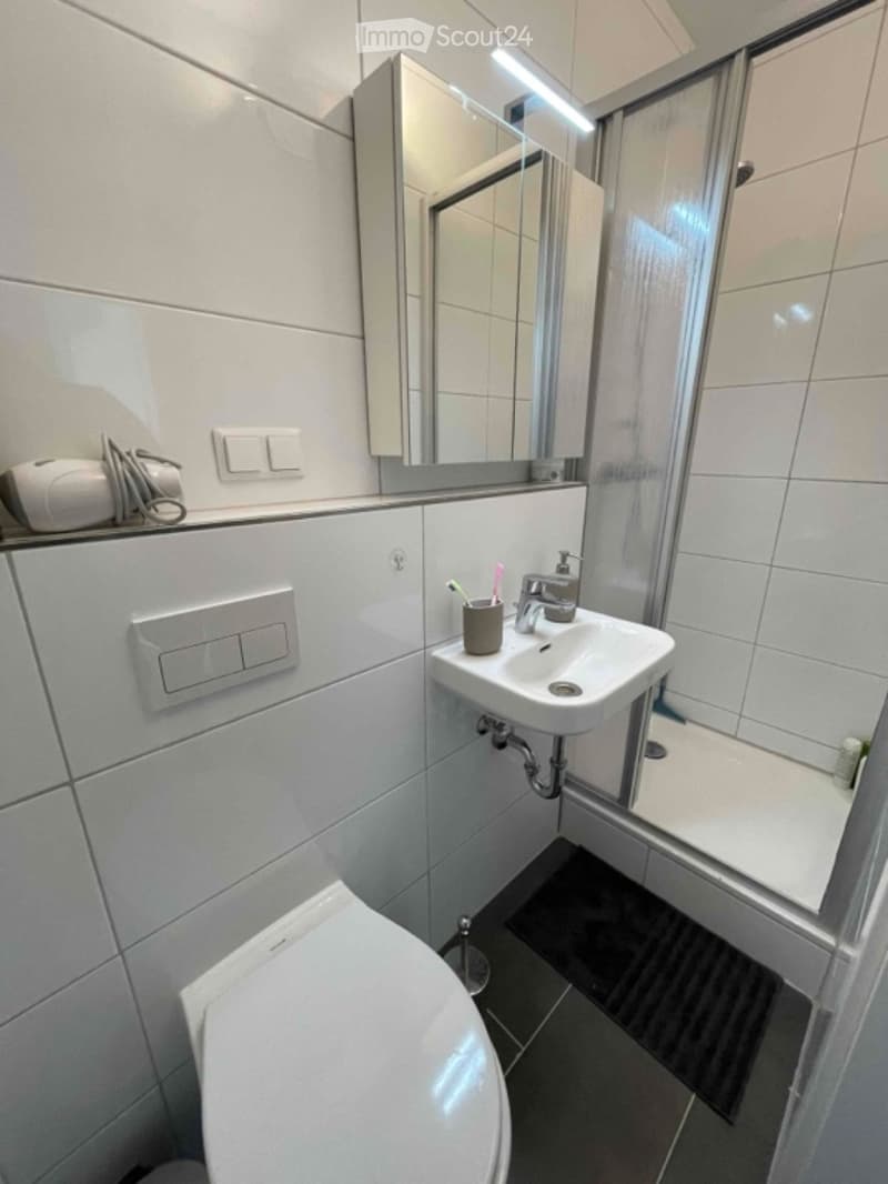 Modern bathroom with white tiles, a toilet, a sink with a mirror above it, and a shower area with a glass door.
