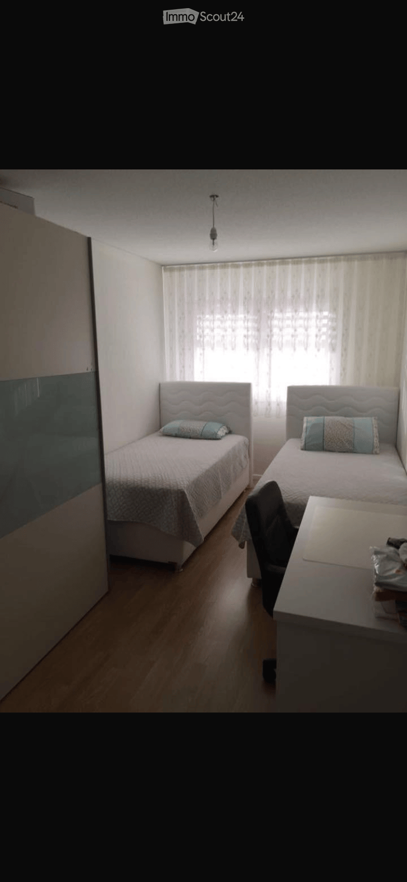 Cozy bedroom with two single beds, matching bedding, a small table with a chair, and a window with sheer curtains.