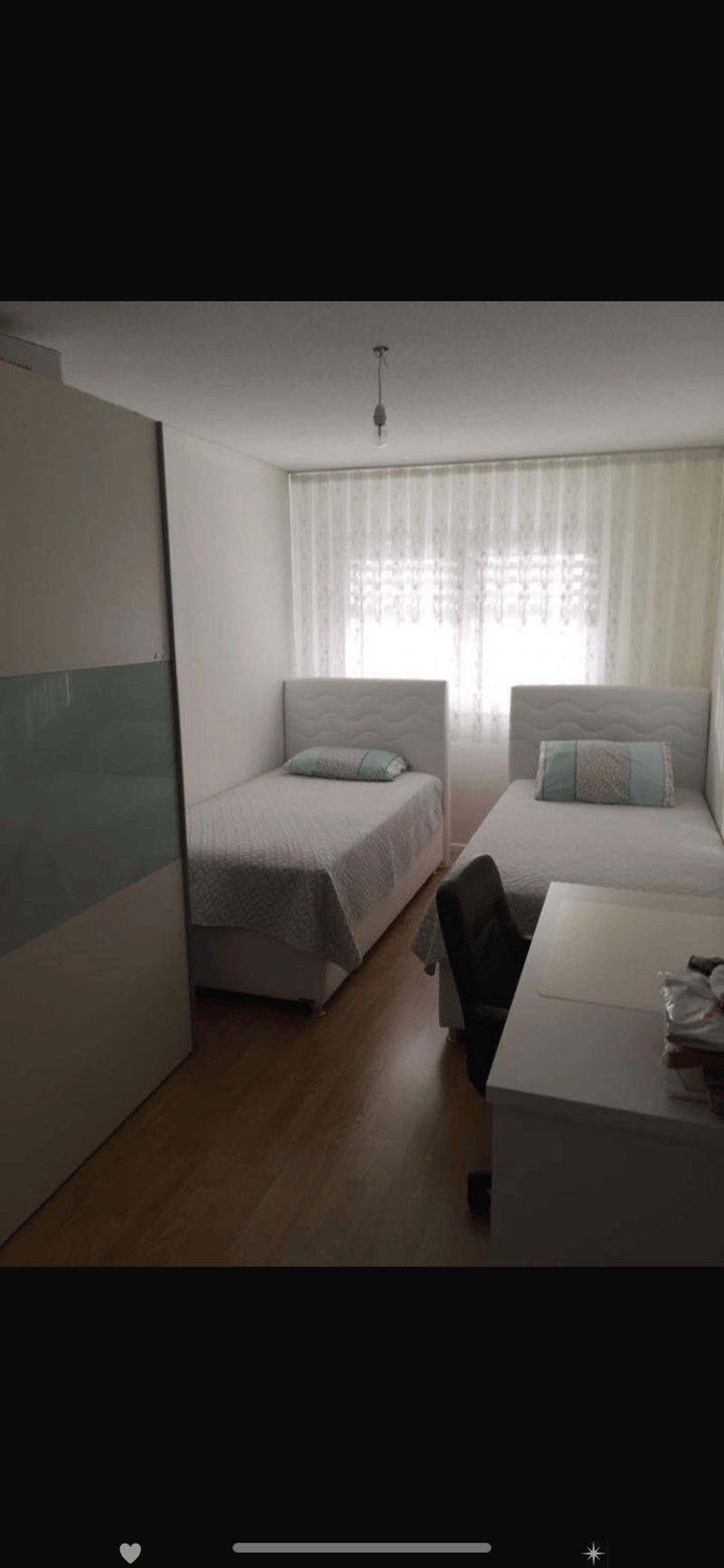 Cozy bedroom with two single beds, a small table, and a chair near the window with curtains.
