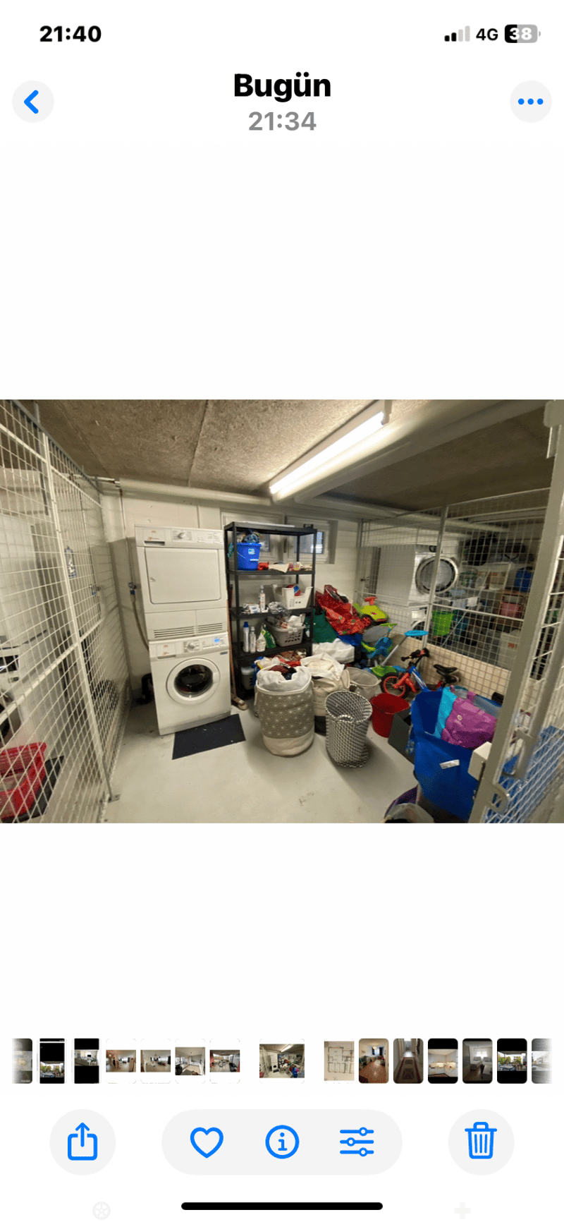 A small, enclosed utility room with a washing machine, shelves, and various storage items including a bicycle and bins.