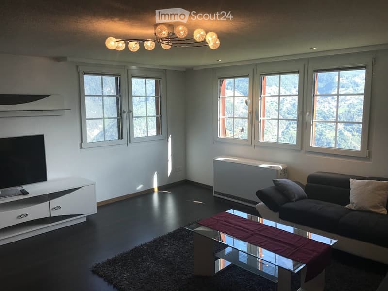 Modern living room with large windows offering a scenic view, a black sofa, a glass coffee table with a red runner, a white TV stand, and a stylish floor lamp.