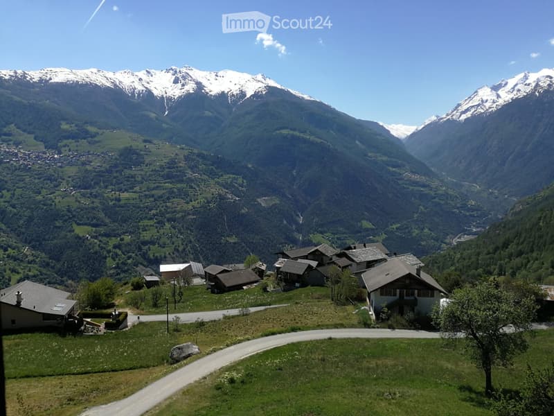 A cluster of houses in a valley surrounded by mountains, with a winding road leading through the area.