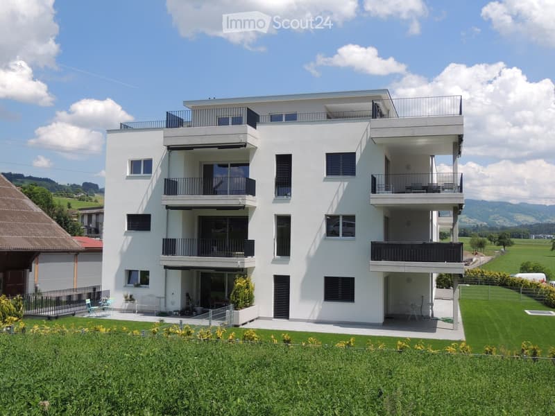 Modern two-story white house with multiple balconies, large windows, and a well-maintained lawn in front.