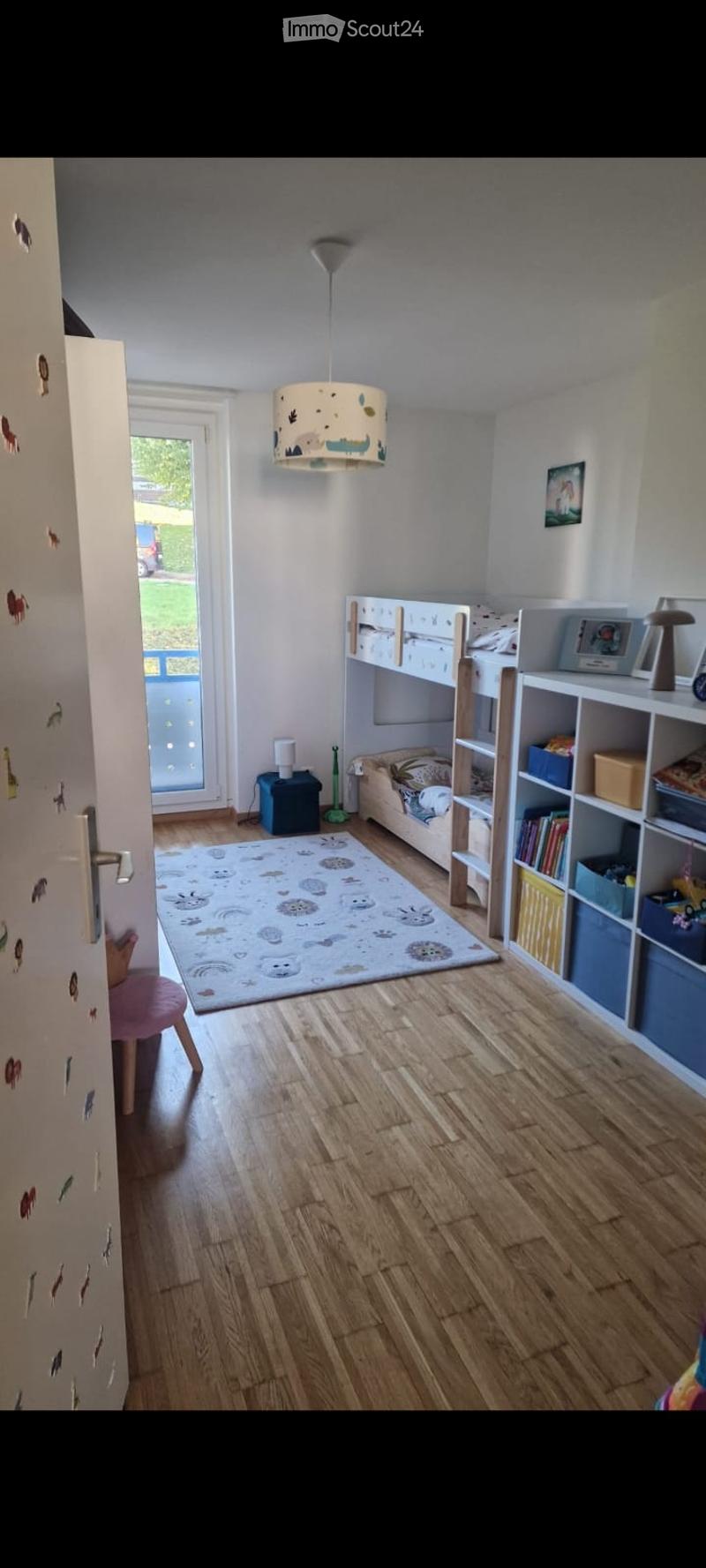 Brightly lit children's bedroom with wooden flooring, bunk bed, bookshelf, small stool, and decorative rug.