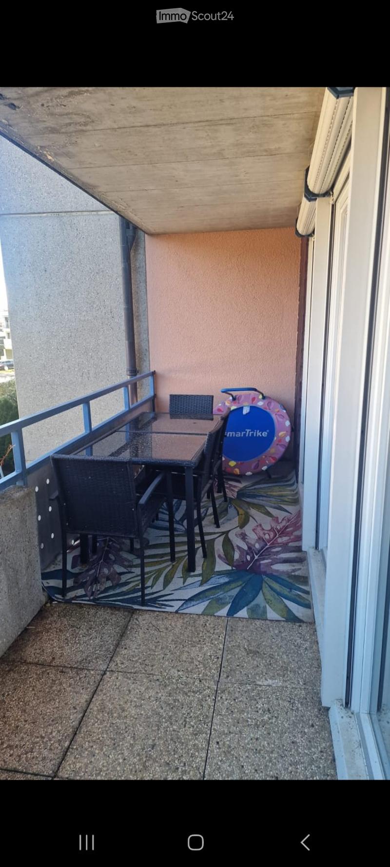 Balcony with a glass table, black chairs, a small stool, and a colorful rug with leaf patterns.