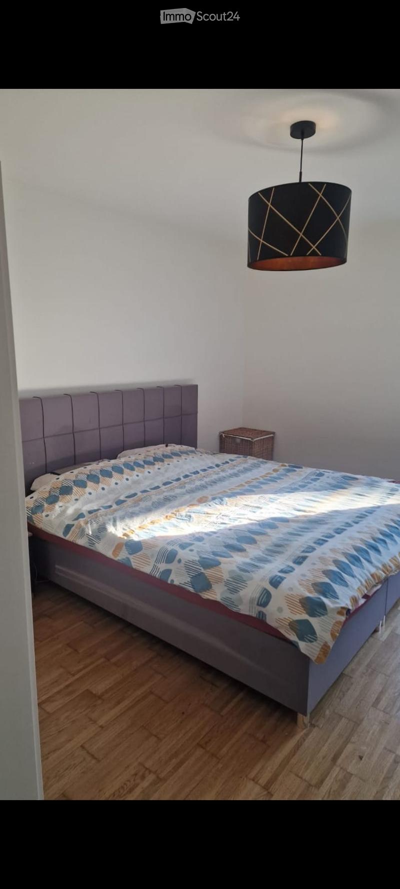 Modern bedroom with a large bed, patterned bedding, a nightstand, and a stylish pendant light fixture.