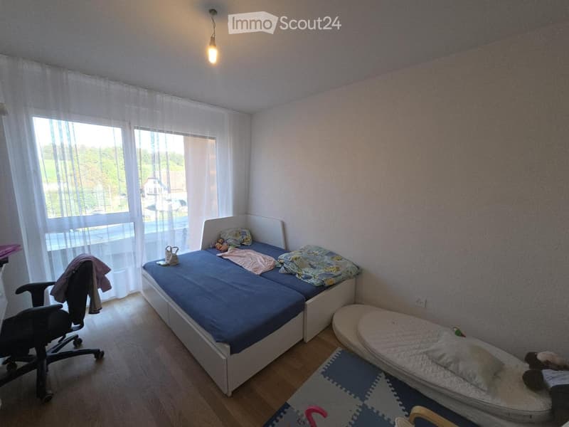 A small bedroom with a single bed, a child's bed, a chair, and a window with curtains.