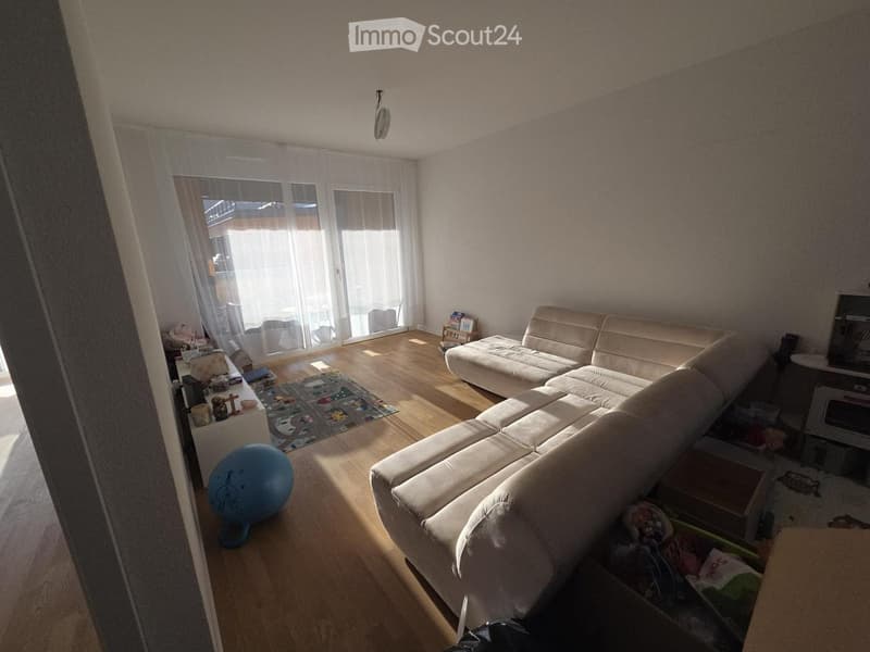 Living room with a large sectional sofa, a blue exercise ball, a small table with various items, and a TV screen in the corner.