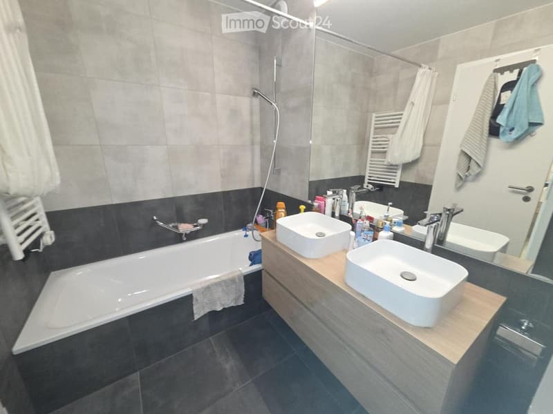 Modern bathroom with a bathtub, double sink vanity, and a large mirror. The space features tiled walls and a wooden vanity with two sinks.