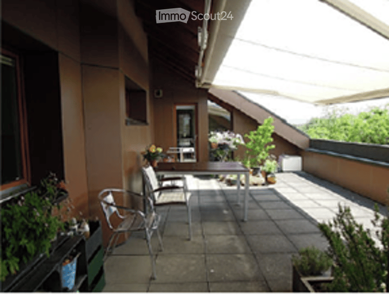 Balcony with tiled floor, outdoor furniture including a table and chairs, potted plants, and a view of greenery.