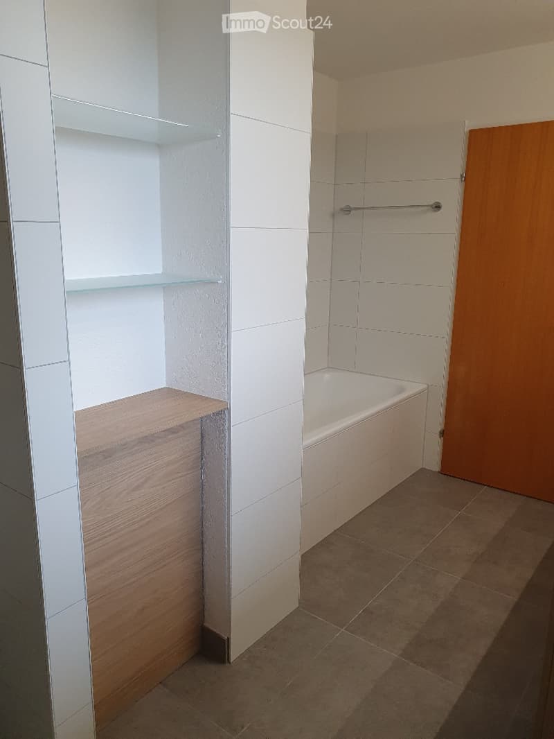 Modern bathroom with a bathtub, wooden shelves, and a towel rack.