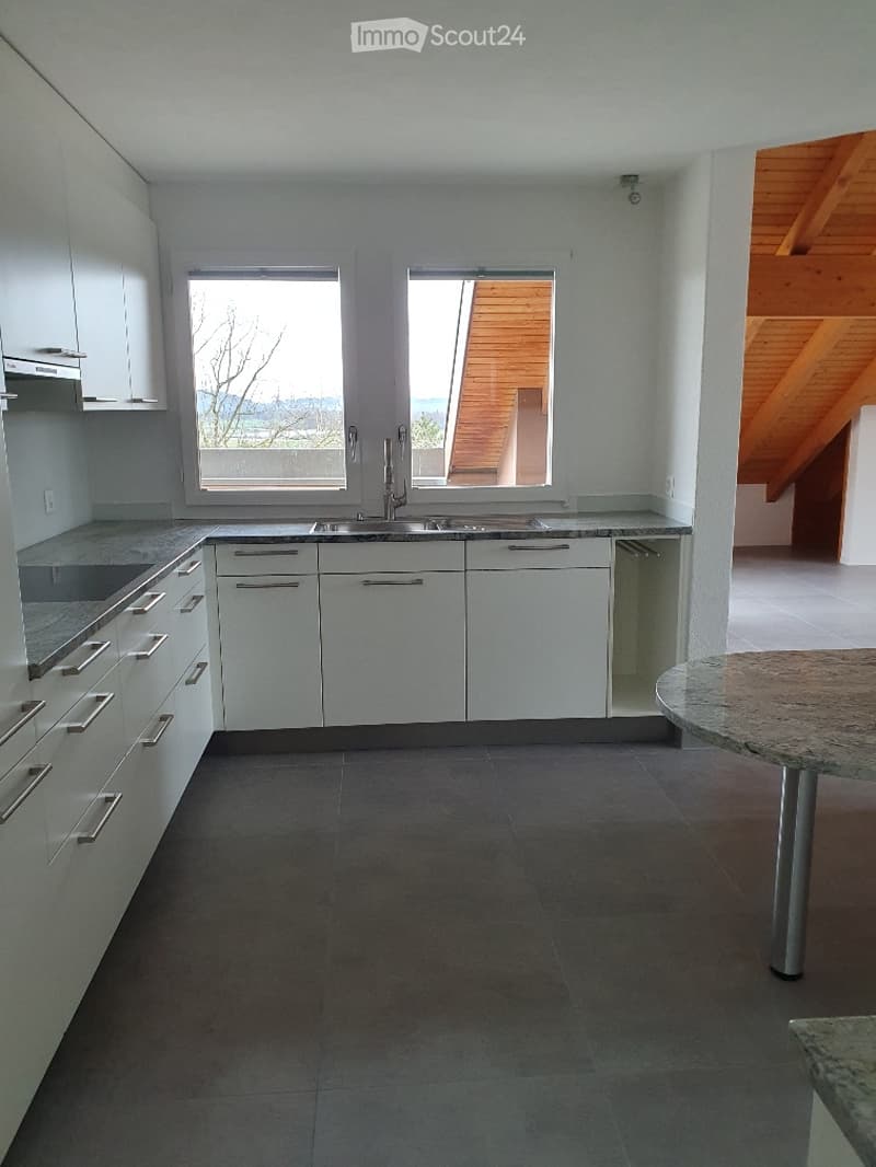 Modern kitchen with white cabinets, stainless steel sink, and granite countertop. Features large windows and a round table with metal legs.