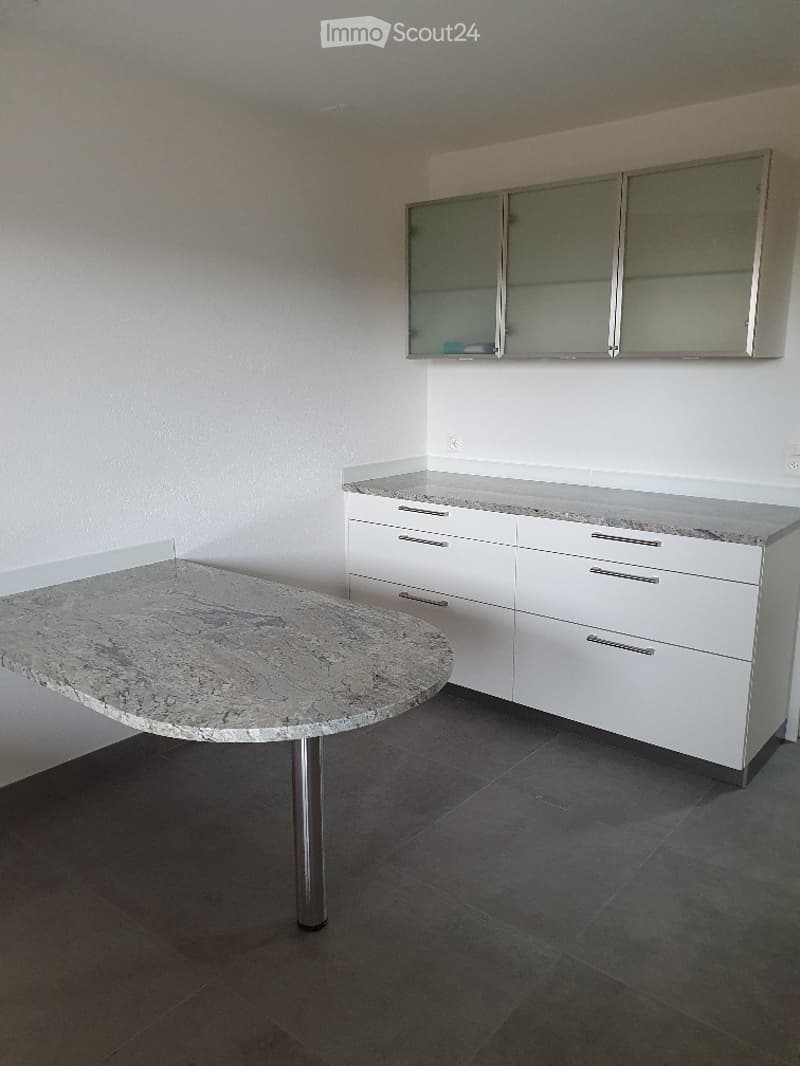 Modern kitchen with white cabinets, granite countertops, and a round table with a metallic base.