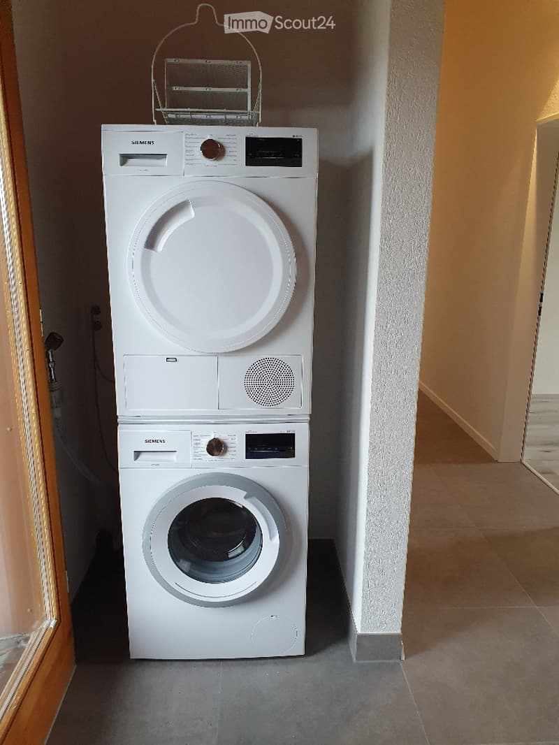 A compact bathroom with a stacked Siemens washing machine and dryer unit, featuring a control panel and a small basket on top.